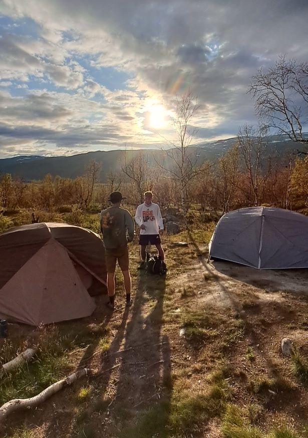 Two tents are pitched in the Kungsleden tundra as the sun sets, casting long shadows across the landscape.