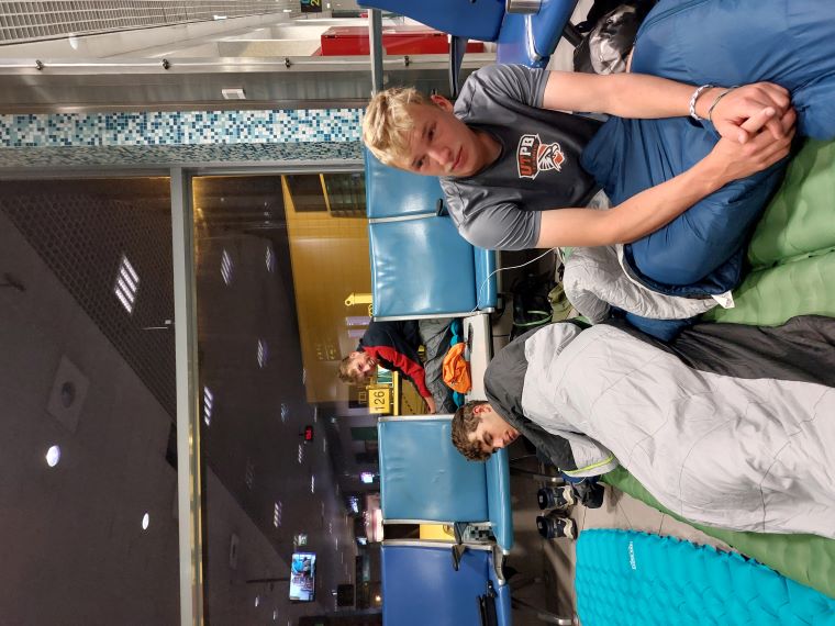 A photo taken by Florian showing the four boys waking up at Lisbon airport after an 8-hour layover, having slept on their ISO mats. They appear visibly tired and not well-rested.