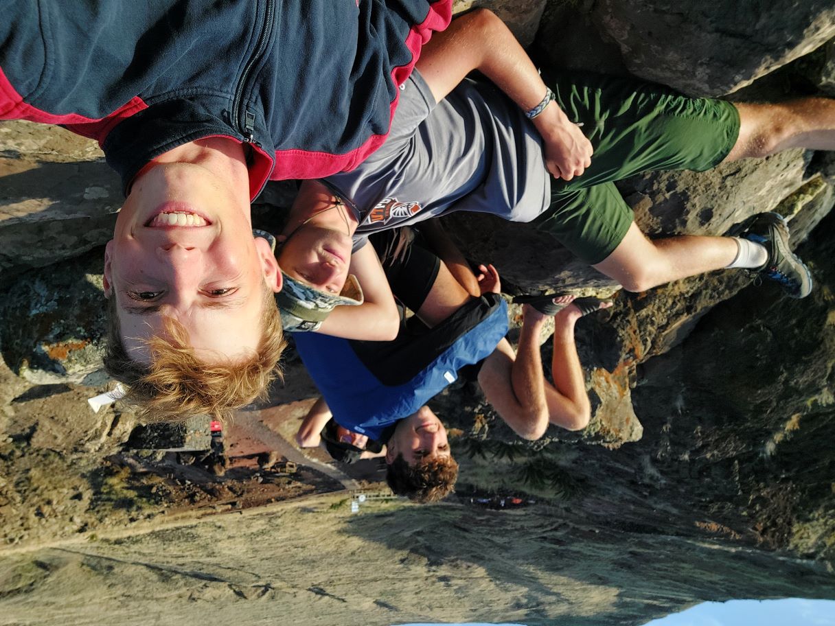 A selfie of four young men—Florian, Maxi, Niki, and Jonas—lying on a large rock in eastern Madeira. They are relaxing after a long day of hiking, watching the sunset together.