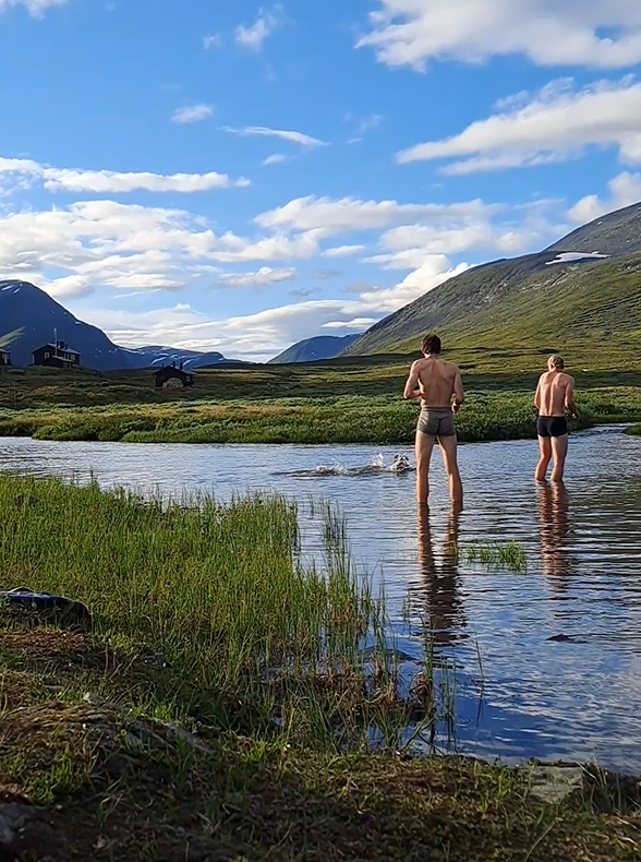 The four boys refreshing themselves in a glacier river along the Kungsleden trail, with icy mountain tops visible in the background.